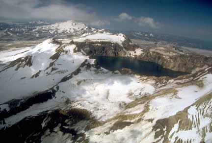 Photograph from air of caldera with lake, some snow, and low clouds