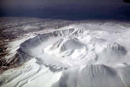 Photograph from air of snow-covered caldera with lava domes in center