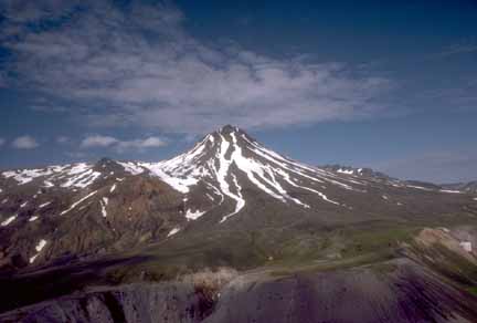 Photograph from the air of partially snow-covered peak with green hills in foreground
