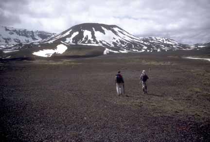 Photograph of two geologists walking away from camera across flats; cone in background