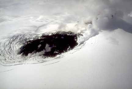 Photograph from air of dark lava flow at base of snow-covered cone; circular fractures in ice exposed