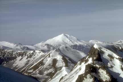 Photograph from air of snow-covered volcanic peak with steep slopes in foreground