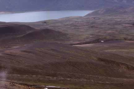 Photograph of tan, ash-covered slopes and lake inside caldera