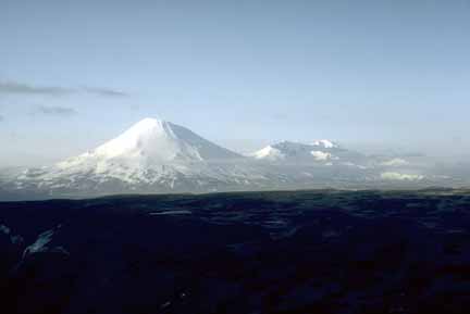 Photograph of symmetrical snow-covered volcano against blue sky, dark foreground