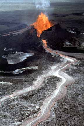 photo 021.  Low-elevation oblique aerial photo of small volcano with red-hot lava fountaining from crater and river of lava flowing from side of volcano