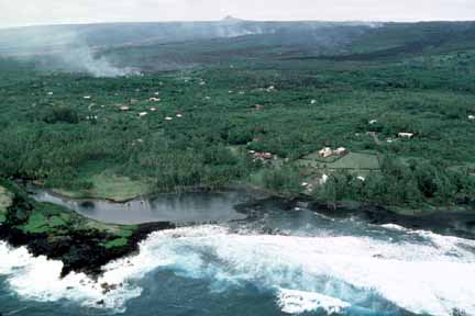 photo 037.  Low-elevation oblique aerial photo of lava flowing from small volcano on horizon through forest in middle ground.  Lagoon and ocean in foreground