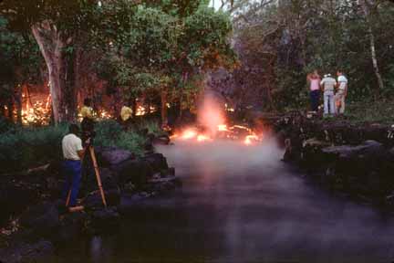 photo 042.  Photo of red-hot lava flowing into what was once a lovely, lush calm pond.  Water is boiling into steam as lava enters.  Surveyors and photographers stand nearby observing