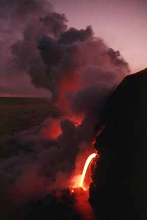 photo 055.  Nighttime photo of spout of lava pouring off cliff into ocean and steam cloud forming.  Cloud is lit from below by glowing lava