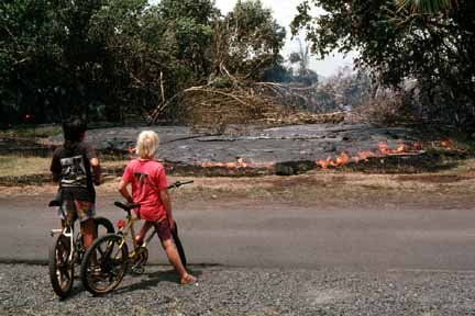 photo 062.  Photo of two barefoot kids and their bicycles in foreground.  Small lava flow progressing in background