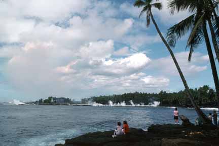 photo 076.  Photo of visitors sitting under palm trees watching lava flow into lagoon in background